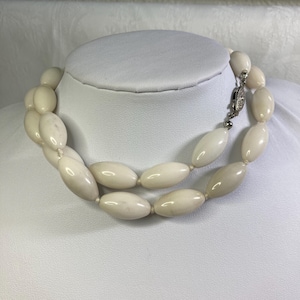 May include: A white oval bead necklace with a silver clasp. The necklace is made of smooth, polished beads and is approximately 18 inches long.