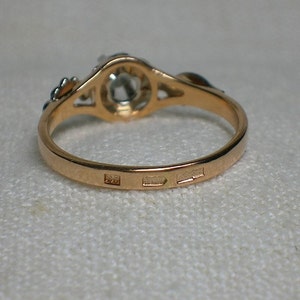 May include: A gold ring with a single round gemstone set in a delicate filigree design. The ring is marked with three hallmarks on the inside band.