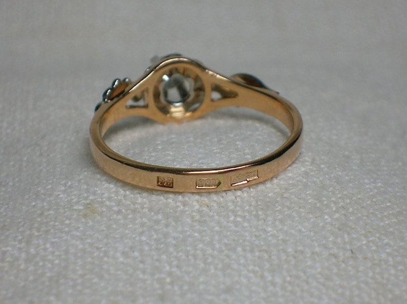 May include: A gold ring with a single round gemstone set in a delicate filigree design. The ring is marked with three hallmarks on the inside band.