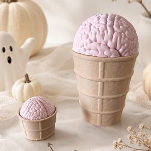 May include: Two light pink brain-shaped objects set inside tan waffle-textured cones. The smaller cone is labeled with the text Clicker and an arrow pointing to it. The brain shapes feature detailed, textured folds resembling human anatomy.