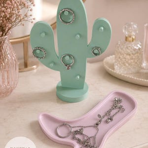 May include: A mint green cactus-shaped ring holder with several rings displayed. A pink, boot-shaped tray holds a silver necklace and ring. The words "DIGITAL PRODUCT" are printed on a white circle.