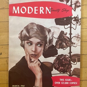 May include: Vintage "Modern Beauty Shop" magazine cover from March 1961. The cover features a woman with a thoughtful expression, surrounded by hats. The magazine's title is in bold white letters on a red banner. The issue had over 123,000 copies.