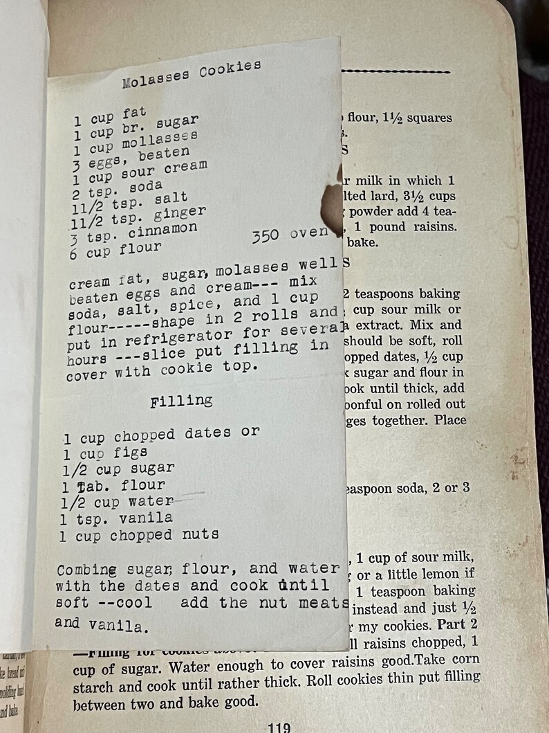 May include: A vintage recipe for Molasses Cookies, with ingredients like molasses, eggs, and spices, is handwritten on a torn piece of paper. The recipe includes instructions for the cookie filling.