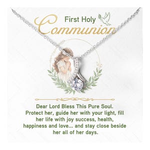 May include: A silver necklace with a pendant featuring a large, clear gemstone. The pendant is set against a backdrop with the words "First Holy Communion" and a prayer. The image includes a dove and a girl.