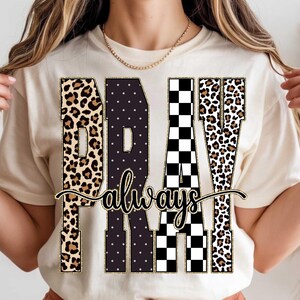 Könnte beinhalten: Cremefarbenes T-Shirt mit dem Schriftzug "PRAY always" in einer dekorativen Schriftart. Die Buchstaben sind eine Mischung aus Leopardenmuster, Tupfen und einem schwarz-weißen Schachbrettmuster. Das Shirt ist ein lässiges Kleidungsstück für den Alltag.