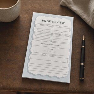 May include: A light blue notepad with a scalloped white center panel featuring the printed text BOOK REVIEW, with sections for book title, author, page length, genres, reading status, a one-sentence summary, rating circles, favorite quote, and review.