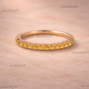 Könnte beinhalten: Ein goldener Bandring mit einem Voll-Eternity-Design. Der Ring ist mit kleinen, runden, gelben Edelsteinen besetzt. Der Ring ist vor einem hellbraunen Hintergrund platziert. Der Text "JewelsByPK" ist im Bild sichtbar.
