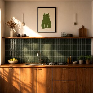 Könnte beinhalten: Eine Küche mit Holzschränken, einem dunkelgrünen Fliesenspiegel sowie einem Edelstahlspülbecken und Herd. Ein gerahmter Druck einer grünen Katze hängt an der Wand über einem Holzregal, auf dem eine Vase, Schalen und ein Schneidebrett stehen.