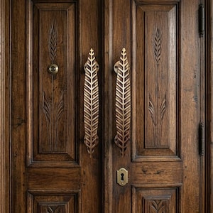 May include: A set of double wooden doors featuring dark brown wood grain, carved wheat stalk motifs, and two vertical brass handles shaped like leaves. A circular brass peephole is on the left door, and a brass keyhole plate is on the right door.