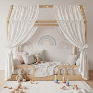 May include: A wooden house-shaped bed frame with white curtains, fairy lights, and pastel pillows. The bed includes a teddy bear, while the floor features a white rug with wooden blocks, stacking rings, and a plush toy rabbit.