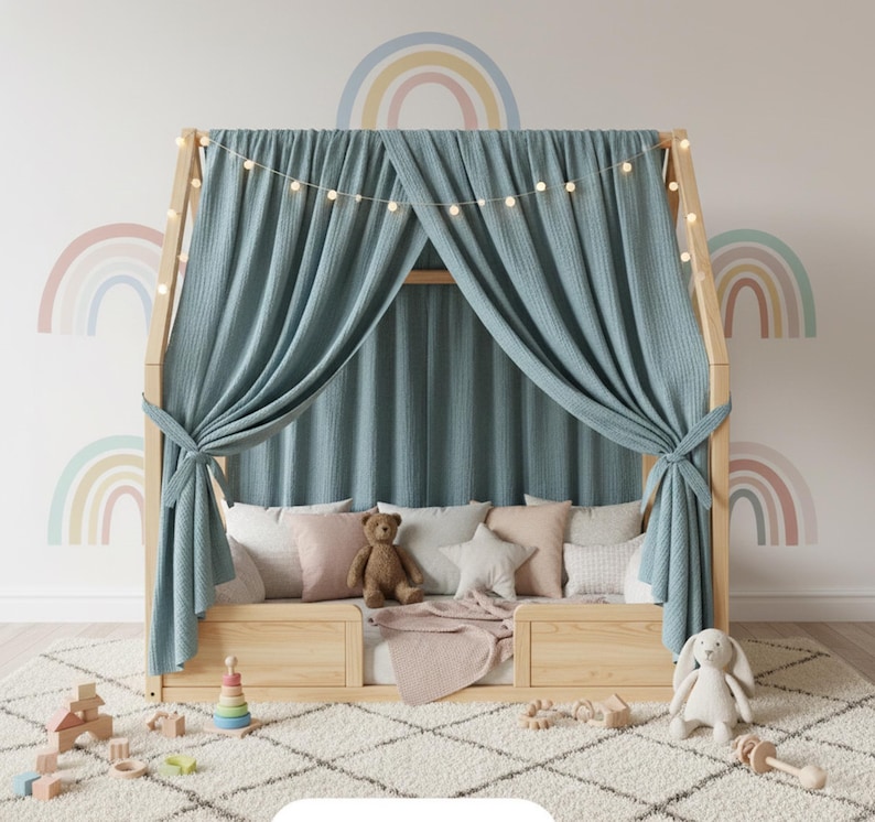 May include: A wooden house-shaped bed frame with a light blue curtain and string lights. The bed is decorated with pillows, a teddy bear, and a blanket. A white rug and toys are in front of the bed.