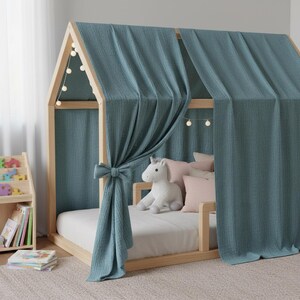 May include: A wooden house-shaped bed frame with a teal fabric canopy and curtains. The bed is furnished with a white mattress, pink pillows, and a stuffed unicorn. A small wooden bookshelf and books are visible.