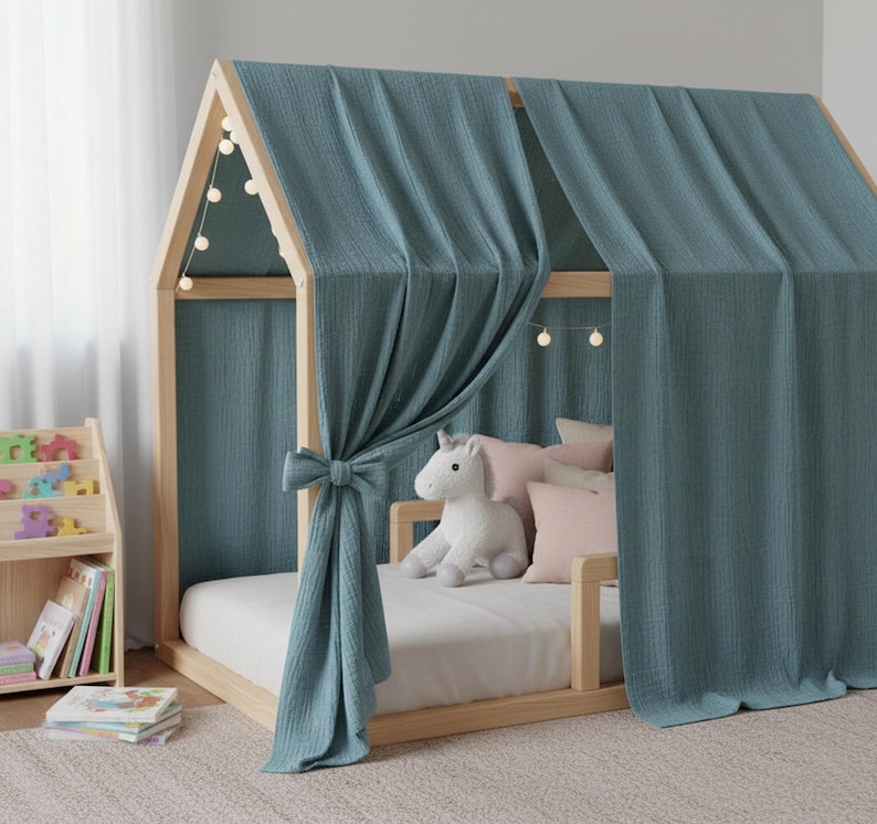 May include: A wooden house-shaped bed frame with a teal fabric canopy and curtains. The bed is furnished with a white mattress, pink pillows, and a stuffed unicorn. A small wooden bookshelf and books are visible.