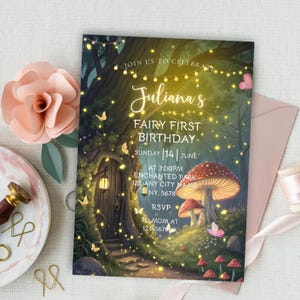 May include: A whimsical fairy-themed birthday invitation with the text "Juliana's Fairy First Birthday." The invitation features a fantasy forest scene with a mushroom, fairy lights, and a fairy door. A pink paper flower and envelope are also visible.