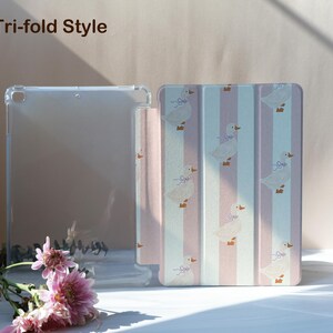 May include: A clear tablet case and a tri-fold style cover. The cover features a pattern of white ducks with purple bows on a pink and white striped background. The text "Tri-fold Style" is visible in the upper left corner.