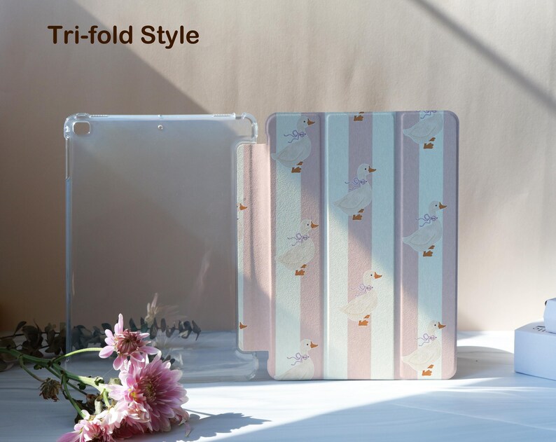 May include: A clear tablet case and a tri-fold style cover. The cover features a pattern of white ducks with purple bows on a pink and white striped background. The text "Tri-fold Style" is visible in the upper left corner.