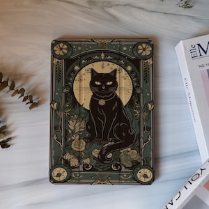 May include: A tablet case with a black cat design. The cat sits before a golden moon, with green and brown floral and botanical details. The case has an elaborate border. The design has an Art Nouveau style.