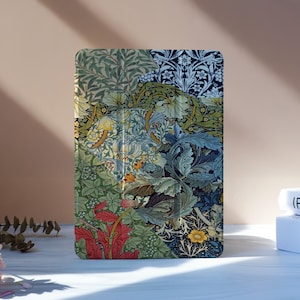 Op de afbeelding: Een tablet hoesje met een kleurrijk bloemenpatroon. Het ontwerp bevat een mix van groene, blauwe, rode en gele botanische elementen. De hoes staat rechtop op een wit oppervlak, met een boek en bloemen op de achtergrond.