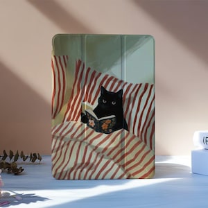 May include: A rectangular tablet case featuring a printed illustration of a black cat reading a book while lying in a bed with red and white striped bedding. The case has a tri-fold design with visible vertical creases across the front surface.