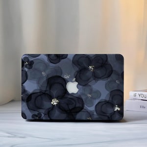 May include: A laptop case featuring a floral pattern. The case is predominantly dark blue, adorned with large, abstract black flowers. The flower centres have gold accents. The Apple logo is visible in the centre of the case.