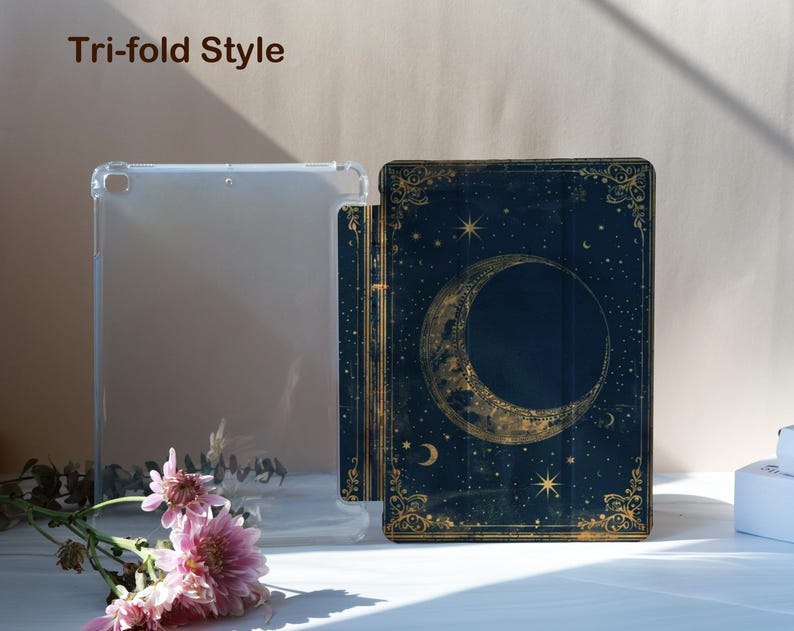May include: A clear, tri-fold style tablet case and a dark blue tablet case with a celestial design featuring a crescent moon, stars, and gold accents. The text "Tri-fold Style" is at the top. Pink flowers are in the foreground.