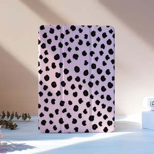 Può includere: Una custodia per tablet rosa chiaro con un motivo leopardato nero. La custodia è in posizione verticale su una superficie bianca, con libri e fiori sullo sfondo. La custodia ha una finitura liscia e lucida.