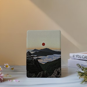 Pode incluir: Uma capa retangular para leitor de e-books com uma estampa gráfica de uma paisagem com montanhas verde-escuras, um mar de nuvens brancas e um sol vermelho sólido centralizado em um céu pálido. O design cobre a frente da capa protetora.