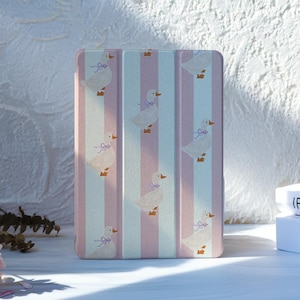 May include: A rectangular tablet case with a vertical striped pattern in pink and white. The case features a repeating pattern of white ducks with purple bows. The case is on a white surface.
