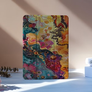 Puede incluir: Una funda de tableta colorida con un diseño abstracto. La funda presenta una vibrante mezcla de tonos turquesa, amarillo, naranja y rojo, creando un patrón artístico y fluido. La funda está de pie, mostrando su diseño único.