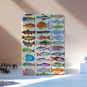 May include: A white tablet case featuring a colorful pattern of various fish illustrations. The fish are depicted in a variety of colors and styles, creating a vibrant and eye-catching design. The case is rectangular and appears to be made of a durable material.
