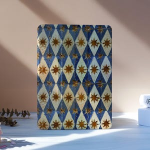 Könnte beinhalten: Eine rechteckige Box mit einem blau-weißen Rautenmuster, verziert mit goldenen Sternenmotiven. Die Box steht auf einer weißen Oberfläche, mit rosa Blumen und Büchern im Hintergrund.
