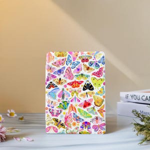 May include: A white rectangular case covered in a colorful butterfly pattern. The butterflies are in various sizes and colors, including pink, blue, yellow, and green. The case is on a white surface.