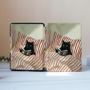 May include: A protective e-reader case featuring a printed illustration of a black cat reading a book whilst tucked into bed with red and white striped bedding. The design shows the cat holding an open book with a floral pattern on the cover.