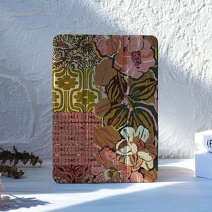 May include: A rectangular tablet case featuring a multi-panel design with a mix of floral and geometric patterns in shades of pink, olive green, mustard yellow, and brown. The surface displays a vertical fold line and a smooth, matte finish.