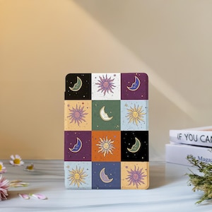 Puede incluir: Una funda cuadrada y multicolor con un diseño celestial. El diseño incluye soles y lunas crecientes en varios colores, dispuestos en un patrón de cuadrícula. La funda tiene un acabado liso y una esquina redondeada.