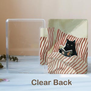 May include: A clear plastic protective case for an e-reader featuring a printed illustration of a black cat reading a book while lying in bed with red and white striped pillows and blankets. The text Clear Back is printed at the bottom.