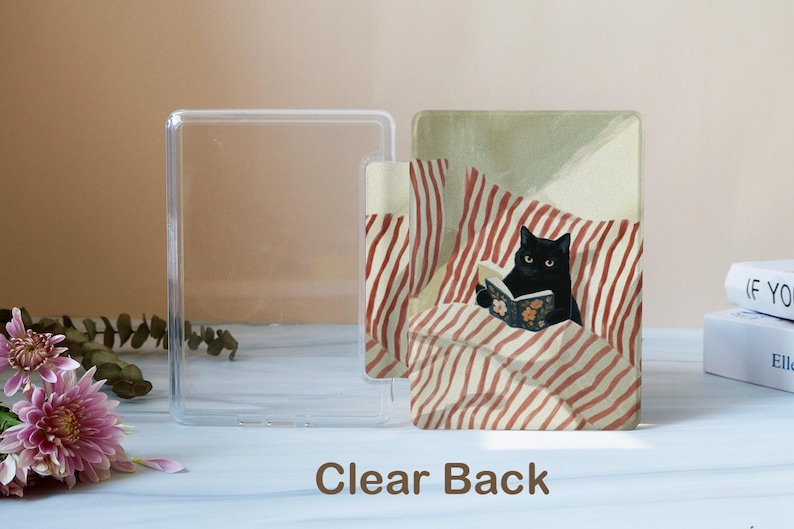 May include: A clear plastic protective case for an e-reader featuring a printed illustration of a black cat reading a book while lying in bed with red and white striped pillows and blankets. The text Clear Back is printed at the bottom.
