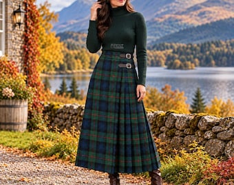 May include: A dark green ribbed turtleneck sweater paired with a floor-length pleated kilt skirt featuring a blue, green, and red tartan plaid pattern. The skirt includes two brown leather side straps with silver buckles at the waist.