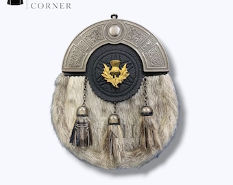 Puede incluir: Un sporran escocés tradicional con un cantle plateado y un cuerpo de piel. El sporran presenta una parte delantera de cuero negro con un emblema de cardo dorado y tres borlas decorativas. El logotipo de Kilt Corner está en la esquina superior izquierda.