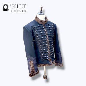 May include: A navy blue military-style jacket with a faux fur collar and trim. The jacket features decorative silver-colored buttons and intricate detailing along the front and sleeves. The Kilt Corner logo is in the upper left corner.
