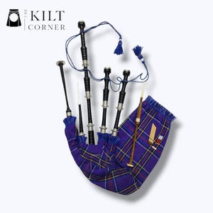 Puede incluir: Una gaita escocesa con una bolsa de tartán púrpura y tubos negros y plateados. La gaita tiene borlas azules y un puntero. El logotipo "The Kilt Corner" es visible.