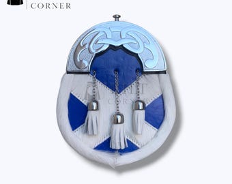 Puede incluir: Un sporran escocés tradicional con cuerpo de piel blanca, detalles en cuero azul y una parte superior de metal plateado. Cuenta con tres borlas blancas y detalles de cadena. El logotipo de Kilt Corner es visible.