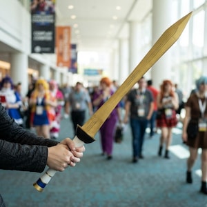A cosplayer holding a custom 3D printed fantasy sword prop indoors at a convention.