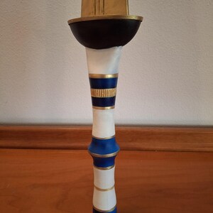 Close-up view of the decorative hilt of a fantasy sword with alternating white, blue, and gold rings and a dark bowl-shaped guard below the golden blade.