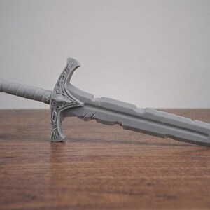 A plain gray unpainted 3D printed short sword replica lying horizontally on a wooden surface.