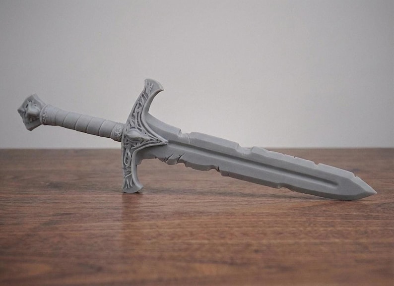 A plain gray unpainted 3D printed short sword replica lying horizontally on a wooden surface.