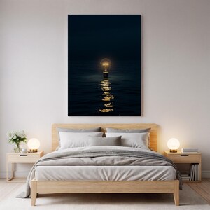 Puede incluir: Una impresión artística enmarcada representa una bombilla brillante flotando sobre agua oscura, con reflejos. La obra de arte está montada sobre una estructura de cama de madera con edredón gris, almohadas y mesitas de noche con lámparas.