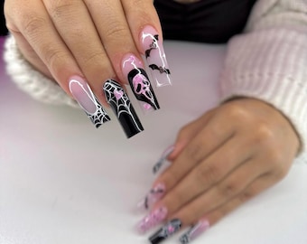 May include: Long, coffin-shaped acrylic nails with a Halloween theme. Designs include a spiderweb, a skull, bats, and pink accents. The nails have a gradient effect, transitioning from clear to pink.