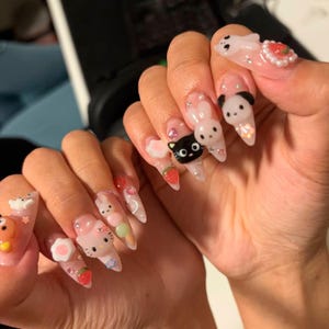 May include: Long, pointed acrylic nails with various 3D designs. The nails feature cartoon characters, strawberries, flowers, and other embellishments. The base color is a clear, glossy finish with glitter accents.