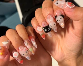 May include: Long, pointed acrylic nails with various 3D designs. The nails feature cartoon characters, strawberries, flowers, and other embellishments. The base color is a clear, glossy finish with glitter accents.